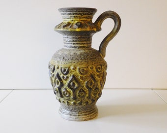 May include: A ceramic vase with a brown and yellow glaze. The vase has a wide mouth and a handle. It is decorated with a geometric pattern.