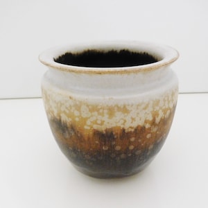 May include: A white ceramic planter with a brown and white speckled glaze. The planter has a rounded shape and a wide opening.