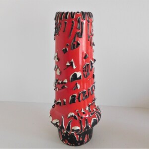 May include: A red ceramic vase with black and white abstract designs. The vase has a flared base and a cylindrical body.