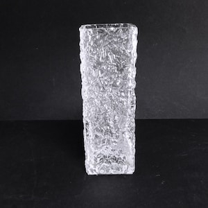 Può includere: Un vaso di vetro trasparente con una superficie testurizzata e smerigliata. Il vaso è di forma rettangolare e ha una base quadrata.