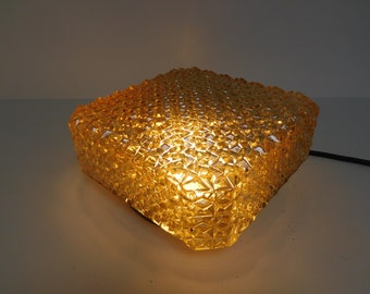May include: A square amber glass ceiling light fixture with a geometric pattern. The light is on and illuminating the room.