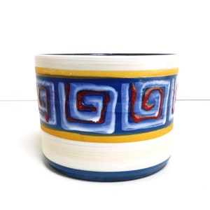 May include: A white ceramic planter with a blue and yellow geometric design. The design features red swirls and squares.