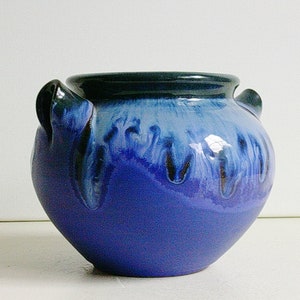Pode incluir: Um pote de cerâmica azul e preto com duas alças. O pote tem um acabamento envidraçado e um design azul e branco manchado.