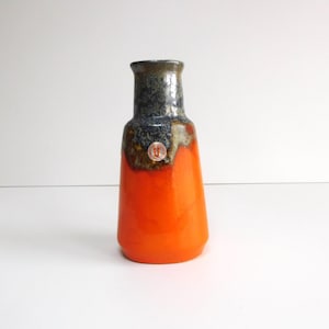 Puede incluir: Jarrón de cerámica naranja y gris con una abertura redonda ligeramente acampanada. El jarrón tiene un esmalte texturizado y una pequeña pegatina redonda en el lateral.
