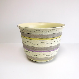 May include: A ceramic planter with a cream-colored interior and a beige exterior. The exterior is decorated with horizontal bands of gray, yellow, and purple, accented with wavy black lines. The planter has a slightly flared rim.