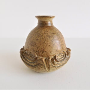 May include: A small, brown ceramic vase with a textured, speckled surface and a decorative, swirling design around the rim.