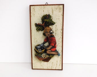 May include: A 3D wall hanging featuring a girl in a red dress feeding birds from a nest. The scene is set against a textured background with a green tree.