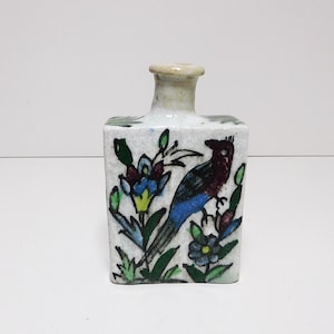 Könnte beinhalten: Kleine, quadratische Keramikvase mit cremefarbenem Hals und weißem Körper. Die Vase ist handbemalt mit einem Vogel, Blumen und Blättern in Blau-, Grün- und Rottönen. Die Vase ist etwa 10 cm hoch.