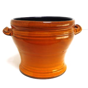 Könnte beinhalten: Ein brauner Keramiktopf mit zwei Griffen. Der Topf hat eine glasierte Oberfläche und einen abgerundeten Boden.