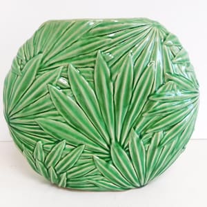 Könnte beinhalten: Eine grüne Keramikvase mit einem einzigartigen Design aus geprägten Palmblättern. Die Vase ist rund und hat eine breite Öffnung.