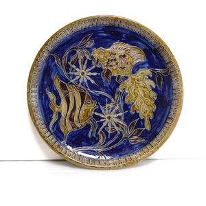 May include: A blue and brown ceramic plate with a decorative design of fish and flowers.