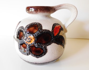 May include: A white ceramic jug with a brown handle and a floral design in shades of brown, orange, and black.
