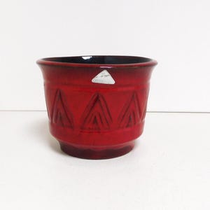 Op de afbeelding: Rode keramische plantenpot met een geometrisch patroon. De pot heeft een zwarte rand en een klein wit label.