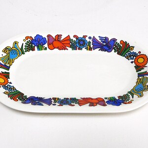 Op de afbeelding: Witte ovale serveerschaal met een kleurrijke rand van gestileerde vogels en bloemen in blauw, oranje, geel en groen. Het keramische gerecht is een decoratief stuk voor het serveren van voedsel.