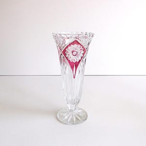 Könnte beinhalten: Eine klare Glasvase mit geschnittenem Kristallmuster und einem rosafarbenen, rautenförmigen Akzent. Die Vase hat eine hohe, schlanke Form und einen ausgestellten Boden.