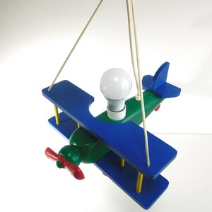 May include: A wooden airplane-shaped ceiling light fitting with blue and green wings, a red propeller, and a white light bulb.