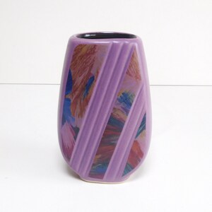 May include: A lavender ceramic vase with a black interior. The vase has a unique shape and is decorated with diagonal stripes and colorful abstract art. The vase is a decorative item.
