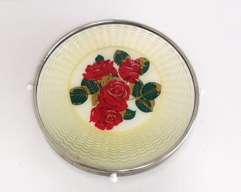 May include: A white ceramic plate with a silver rim and a floral design featuring red roses and green leaves. The plate has a yellow wavy pattern around the edge.