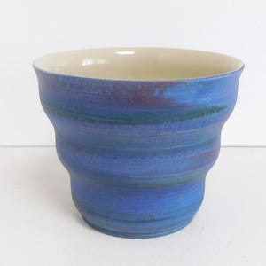 May include: A blue and white ceramic cup with a wavy design. The cup is glazed with a light blue and white glaze, and the glaze has a subtle shimmer.