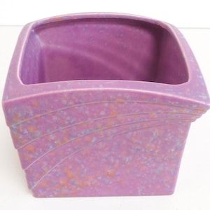 May include: A square ceramic planter with a purple glaze and a speckled pattern. The planter has a slightly curved rim and a geometric design.