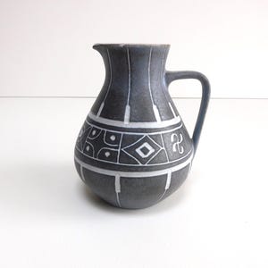 May include: A dark gray ceramic pitcher with a handle and spout. The pitcher features white geometric patterns, including lines, diamonds, and other shapes. The pitcher is likely used for serving beverages.