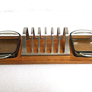 Puede incluir: Una bandeja de servir de madera con dos platos de vidrio y un tostador de metal. La bandeja es de madera marrón claro y los platos son de vidrio transparente.