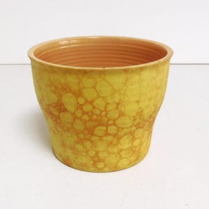 Op de afbeelding: Een gele keramische plantenpot met een bubbelglazuurpatroon. De pot heeft een afgeronde vorm en een glad, licht getextureerd oppervlak.