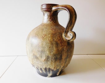 May include: A brown and beige ceramic pitcher with a unique, curved handle. The pitcher has a drip glaze effect and a dark brown base.