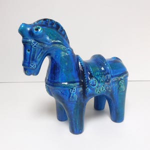 May include: A blue ceramic horse figurine with white details. The horse is standing on all four legs and has a saddle and bridle.