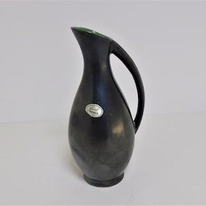 May include: A black ceramic pitcher with a green rim and a silver label that reads "Kunst Keramik".