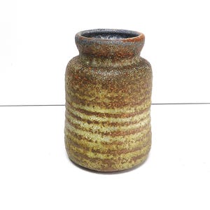 Puede incluir: Un jarrón de cerámica marrón y verde con una superficie texturizada. El jarrón tiene una boca ancha y un cuerpo redondeado.