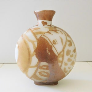 Könnte beinhalten: Eine weiße Keramikvase mit brauner Glasur und einem stilisierten Design. Die Vase hat einen runden Körper und einen schmalen Hals.