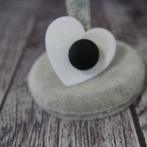 May include: A white heart-shaped ring holder with a black button in the center.