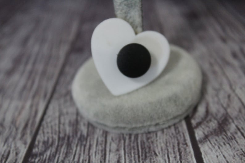 May include: A white heart-shaped ring holder with a black button in the center.
