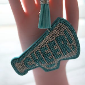 May include: Teal blue megaphone keychain with rhinestones and a teal blue tassel.