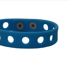 May include: A bright blue silicone wristband featuring a series of evenly spaced circular cutouts along the entire length of the band. The wristband includes two small, circular, metallic-colored snap fasteners positioned near the center.