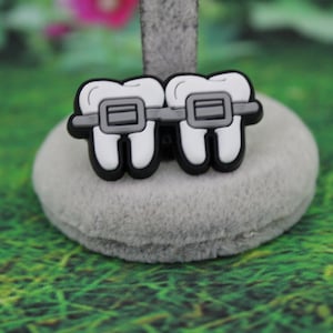 May include: Two white teeth with black outlines and gray braces. The teeth are attached to a gray surface.