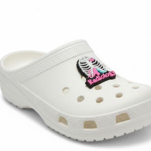 May include: White clog shoe with a Radiology charm. The charm features a black background with a pink and white skeleton design and the word "Radiology" in pink.
