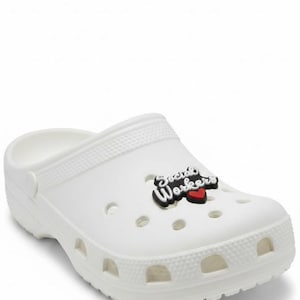May include: White clogs with a decorative charm that reads "Social Workers" in black and white lettering, with a red heart. The clogs have multiple ventilation holes and a textured surface.