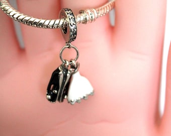 May include: A silver charm bracelet with a charm featuring a black and white tuxedo and a white wedding dress. The charm is attached to a silver ring with a black and silver beaded accent.