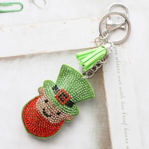 Llavero con diamantes de imitación en forma de duende del Día de San Patricio. Un llavero con brillantes adornos verdes y rojos para carteras, mochilas y llaves de coche.