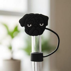 May include: A black pug-shaped straw topper with a clear straw. The pug has white eyes and a sad expression. The straw topper is made of rubber and is attached to a clear plastic straw.