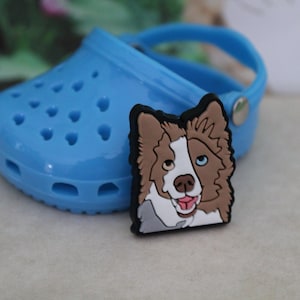 May include: A blue and white cartoon border collie dog charm with a brown and white fur pattern. The charm is made of rubber and has a hole in the back for attaching to a shoe or bag.