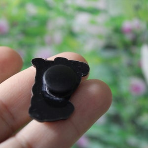 May include: The back of a black metal pin with a round magnet on the back.