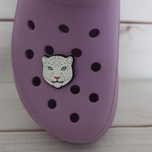 May include: A purple shoe with a white snow leopard face charm attached to it.