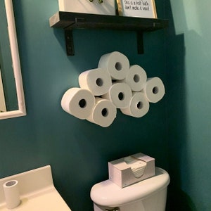 May include: A bathroom with a teal wall and a white toilet. There are eight rolls of toilet paper stacked in a cloud shape on the wall. There is a box of tissues on the toilet tank. The text on the wall says "this is a half bath, don't make it weird."
