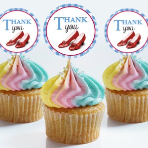 Może przedstawiać: Trzy babeczki z tęczową polewą, ozdobione okrągłymi topperami do babeczek z napisem "Dziękuję" przedstawiającymi czerwone rubinowe pantofelki i wzór w niebiesko-białą kratę.