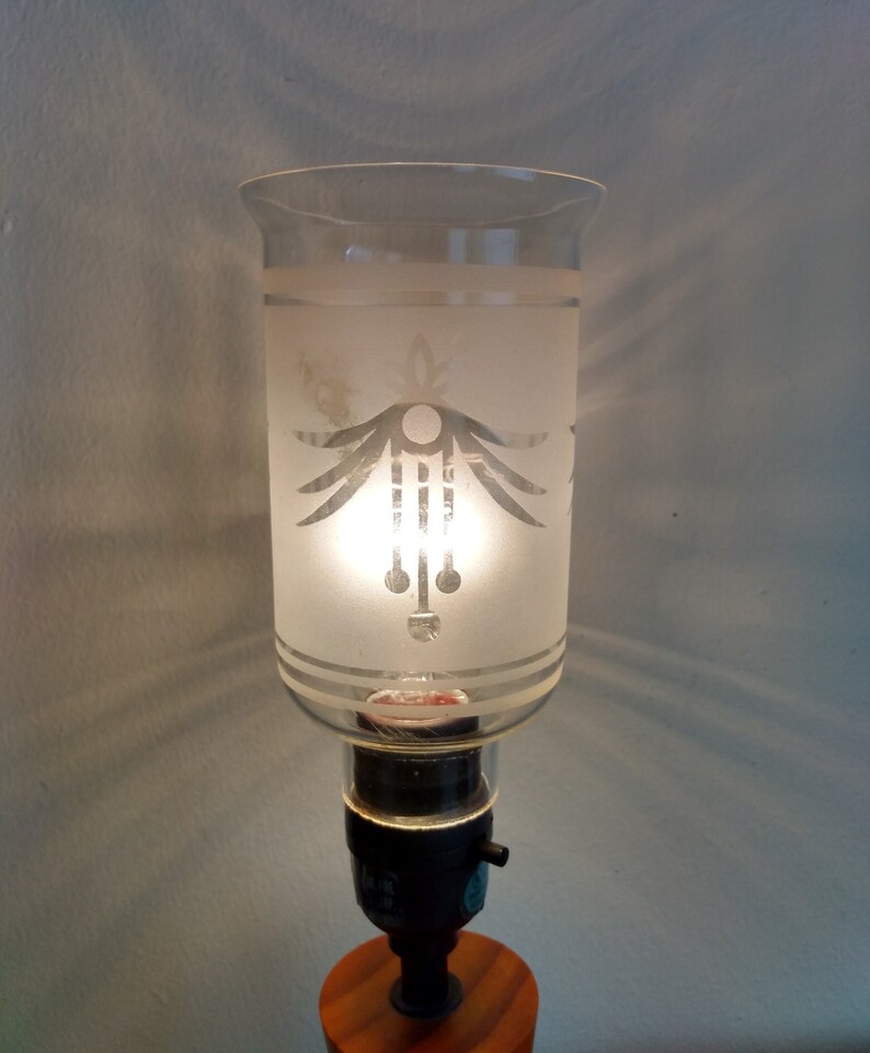 May include: A frosted glass lampshade with a geometric design, featuring a white circle and lines, sits atop a black lamp base with a wooden base.