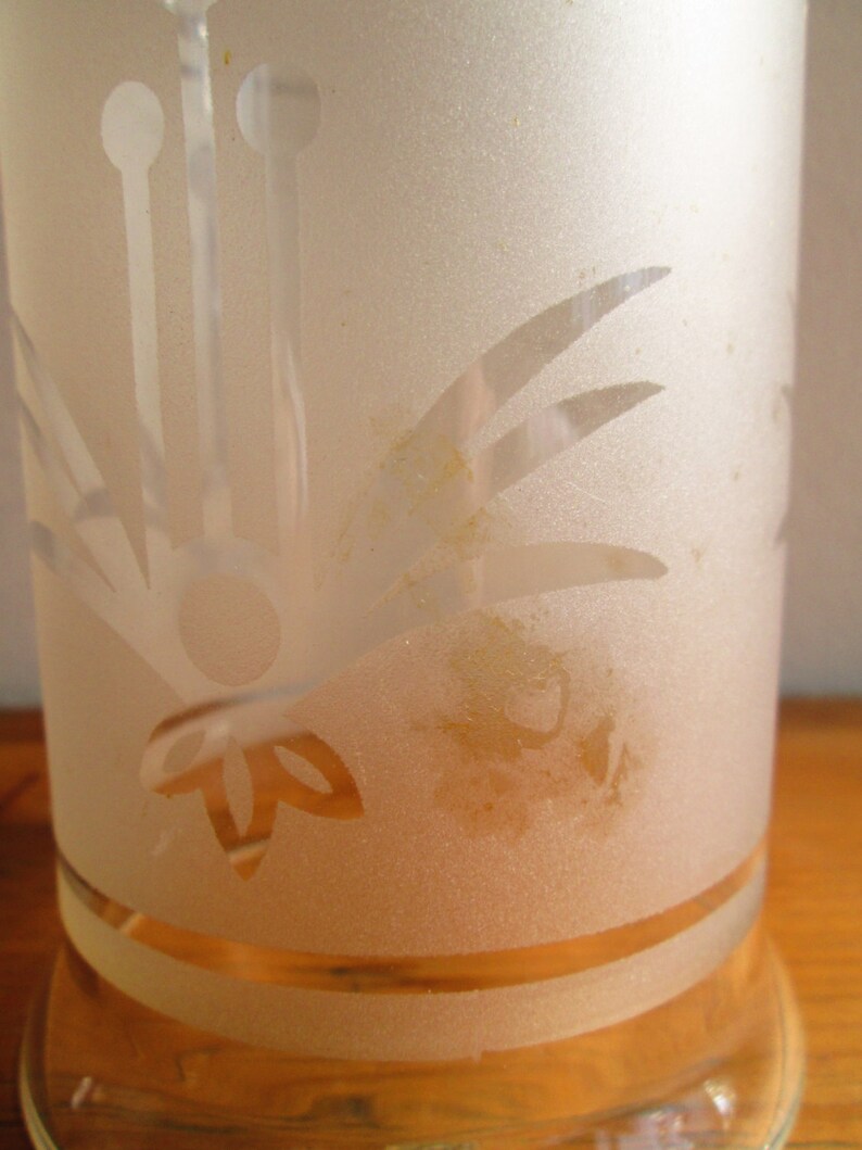 May include: A frosted glass vase with a floral design etched into the surface. The vase has a clear glass base and a frosted glass top. The vase is decorated with a floral design that includes leaves and stems.