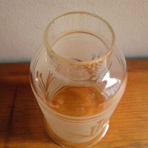 May include: A clear glass bottle with a frosted finish and a decorative design. The bottle has a wide mouth and a rounded bottom.